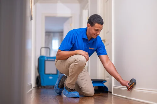 Water damage technician inspecting moisture levels in a residential hallway